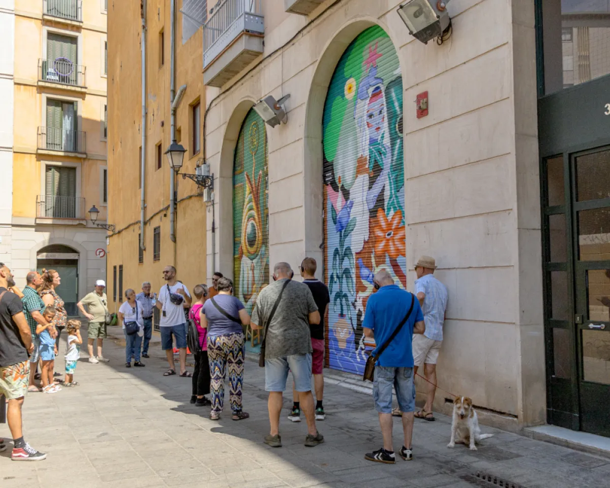 Un grup de persones de diverses edats observa un grafitti pintat sobre una persiana al barri del Raval.