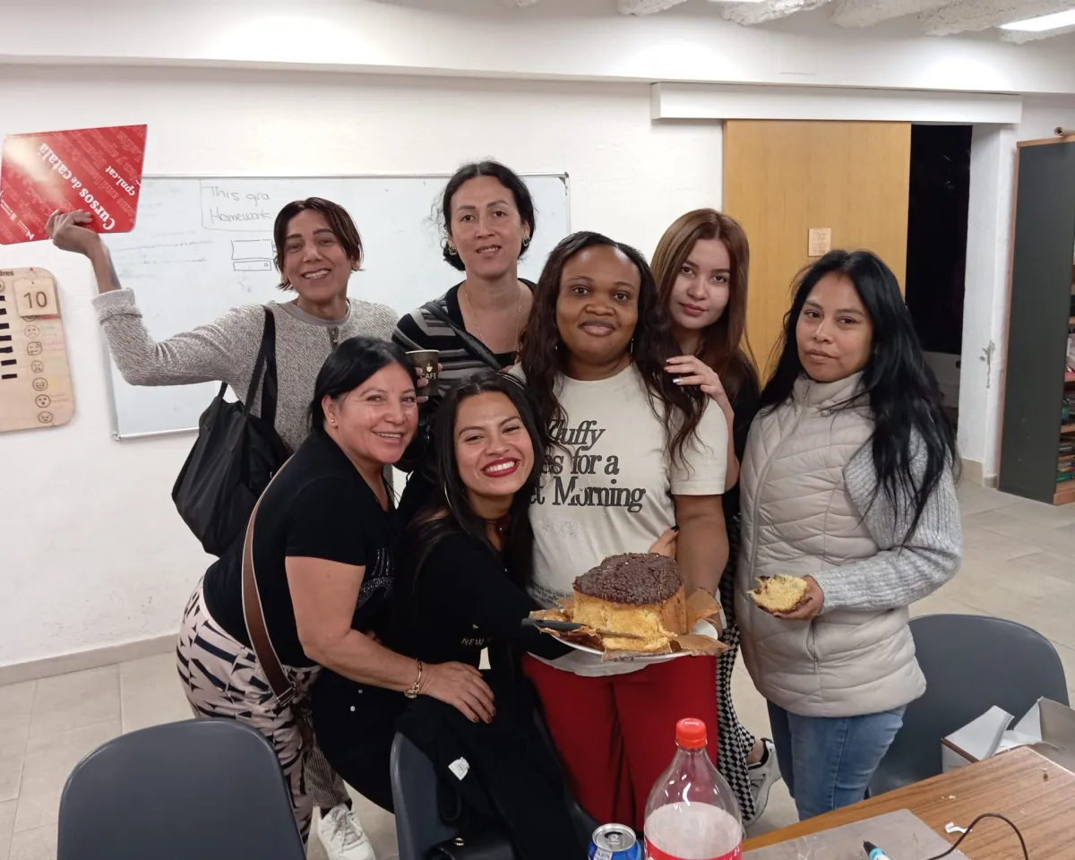 Un grup de dones participant s del projecte Wemin Raval miren a càmera somrients mentre sostenen un pastís.